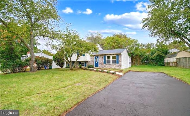 split level home featuring aphalt driveway, stone siding, a front yard, and fence