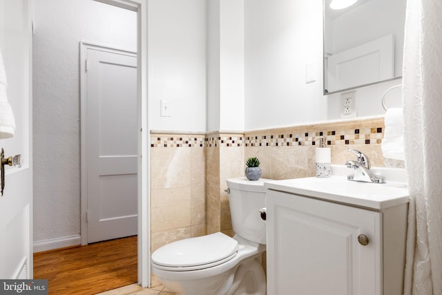 bathroom with a wainscoted wall, toilet, wood finished floors, tile walls, and vanity