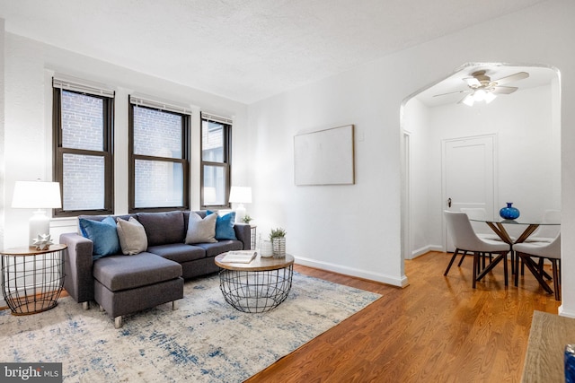 living room featuring a ceiling fan, wood finished floors, baseboards, arched walkways, and a textured ceiling