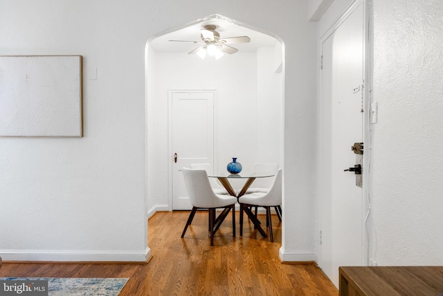 interior space with a ceiling fan, wood finished floors, arched walkways, and baseboards