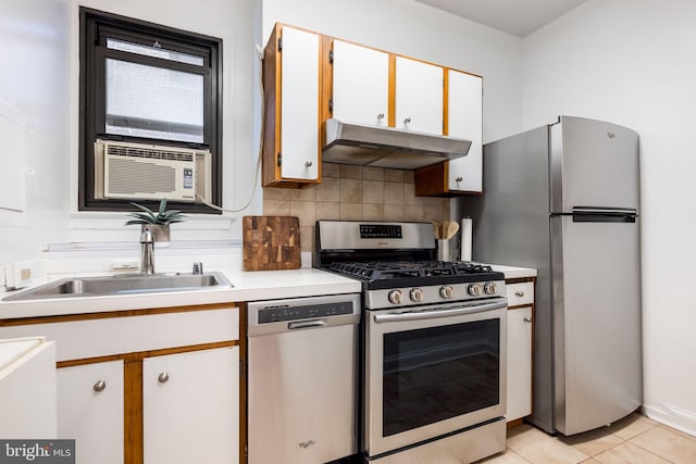 kitchen with under cabinet range hood, a sink, backsplash, stainless steel appliances, and light tile patterned flooring