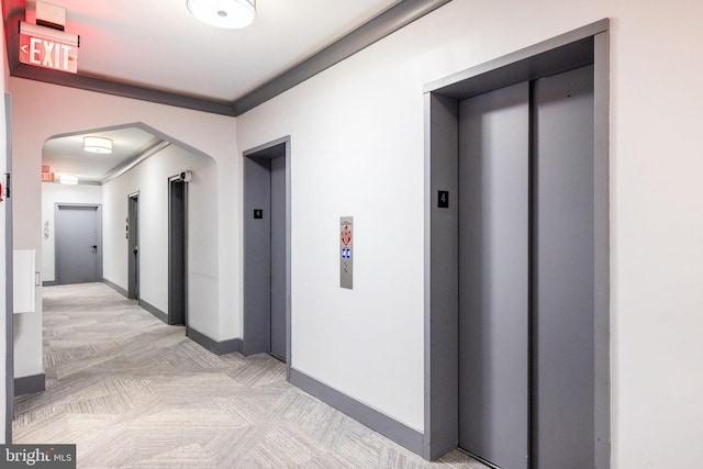 hallway with baseboards, elevator, and arched walkways