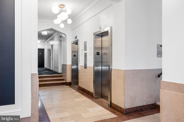 corridor with elevator, wainscoting, arched walkways, and ornamental molding