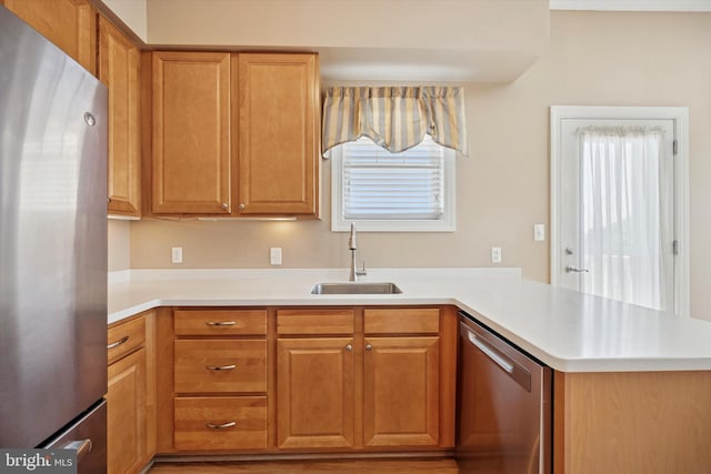 kitchen featuring light countertops, appliances with stainless steel finishes, a peninsula, brown cabinetry, and a sink