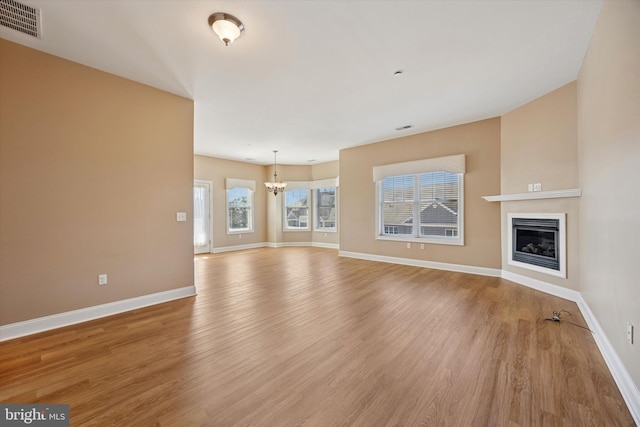 unfurnished living room featuring visible vents, light wood-style flooring, baseboards, and a glass covered fireplace