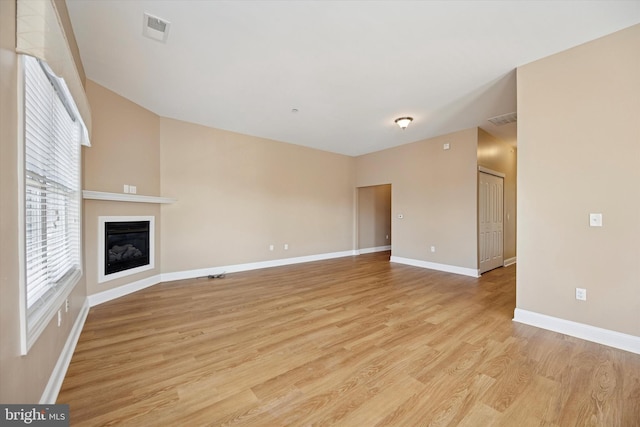 unfurnished living room with a glass covered fireplace, light wood-style flooring, baseboards, and visible vents