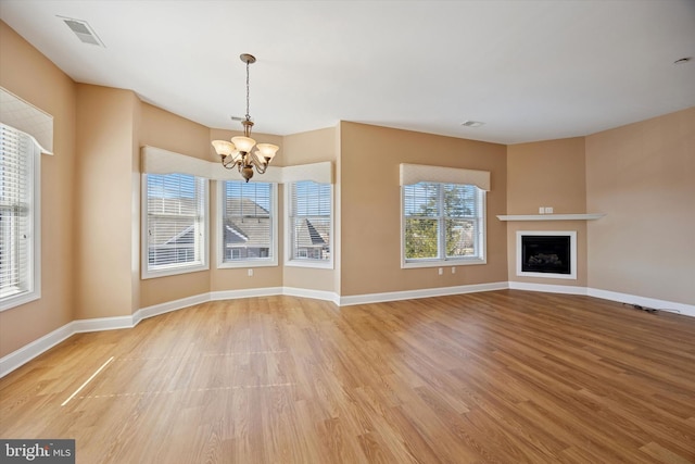 unfurnished living room with visible vents, light wood finished floors, baseboards, an inviting chandelier, and a fireplace