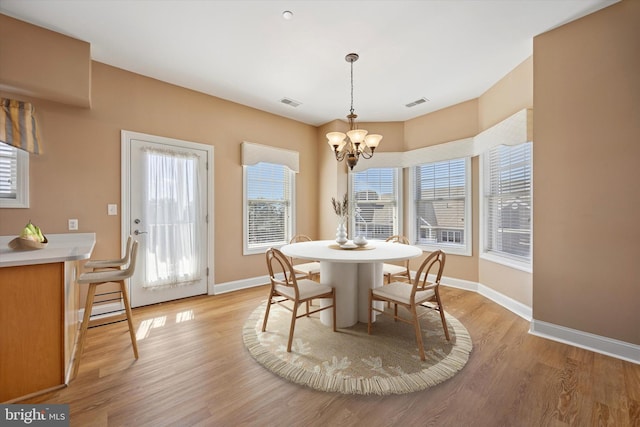 dining space with light wood finished floors, a chandelier, baseboards, and visible vents