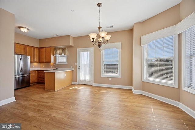 kitchen featuring visible vents, a sink, freestanding refrigerator, brown cabinetry, and light countertops