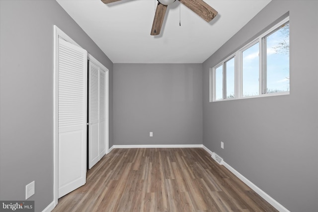 unfurnished bedroom featuring a closet, baseboards, wood finished floors, and a ceiling fan