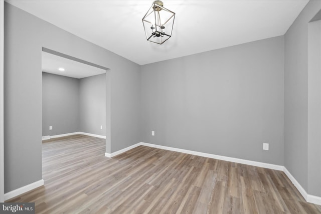 spare room with an inviting chandelier, wood finished floors, and baseboards