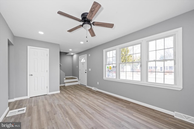 unfurnished living room featuring wood finished floors, stairway, baseboards, and visible vents