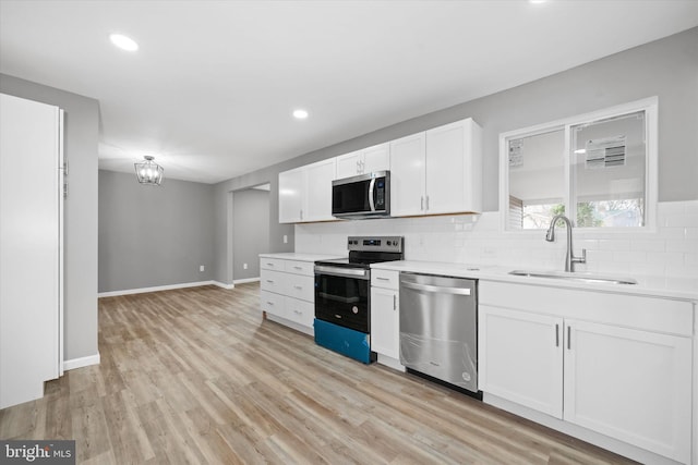 kitchen with light wood-type flooring, a sink, backsplash, stainless steel appliances, and light countertops