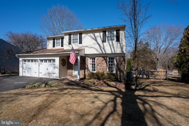 traditional-style house with brick siding, an attached garage, aphalt driveway, and a front yard