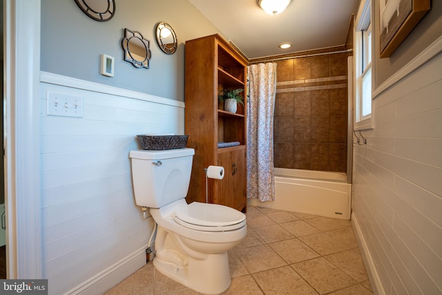 bathroom with tile patterned floors, a wainscoted wall, shower / bathtub combination with curtain, and toilet