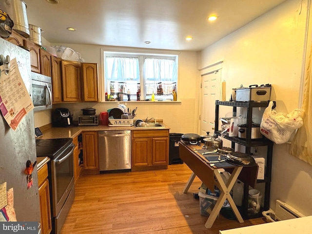 kitchen with light wood-type flooring, recessed lighting, brown cabinets, stainless steel appliances, and a sink