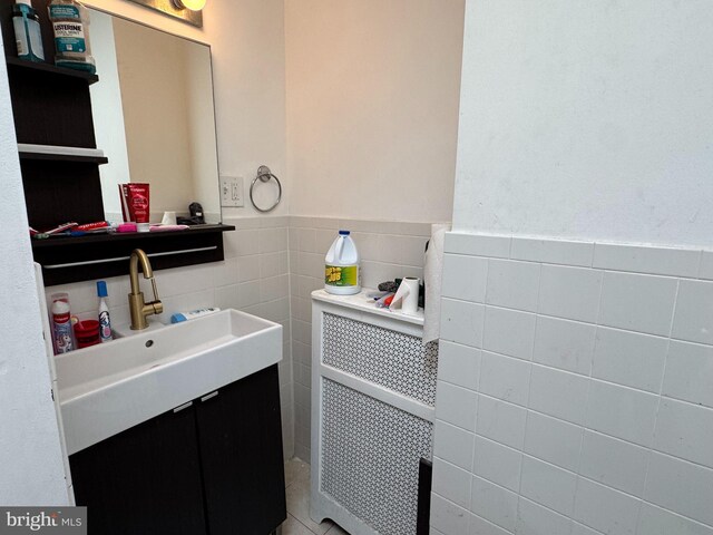 half bathroom with vanity, tile walls, radiator, and a wainscoted wall