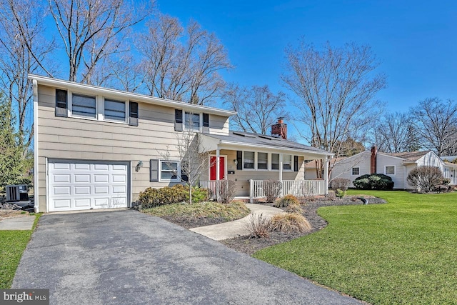 tri-level home featuring driveway, a porch, a front yard, a garage, and a chimney