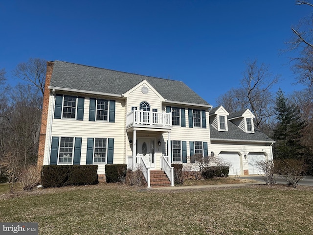 colonial inspired home with a front yard, a balcony, driveway, a shingled roof, and a garage