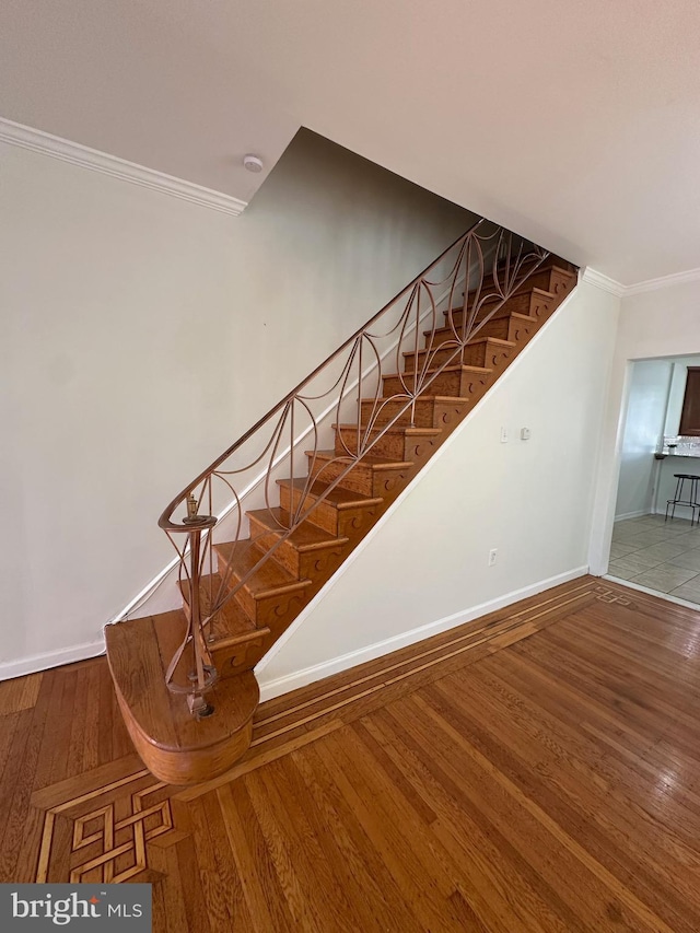 staircase with baseboards, wood-type flooring, and ornamental molding