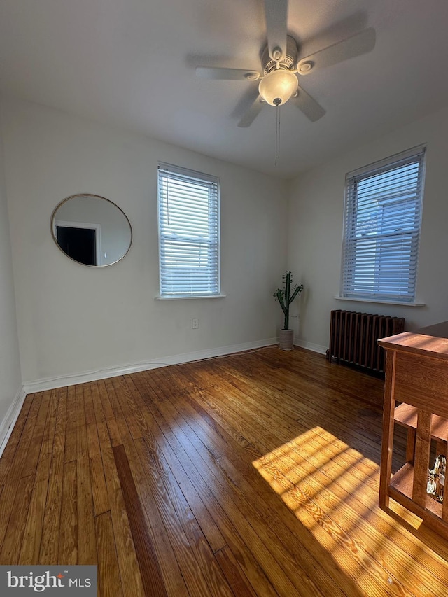 empty room featuring baseboards, wood-type flooring, radiator, and ceiling fan