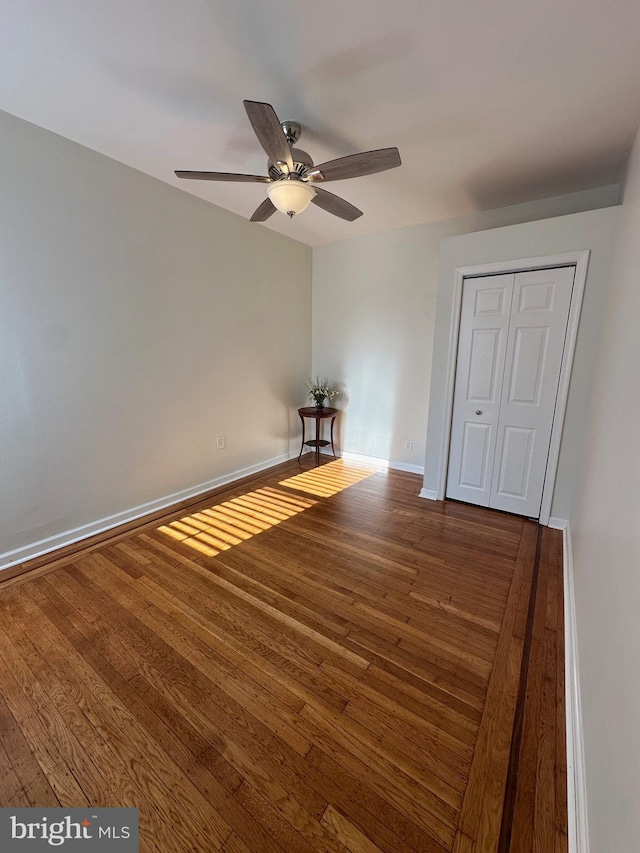 unfurnished bedroom featuring a closet, baseboards, wood finished floors, and a ceiling fan