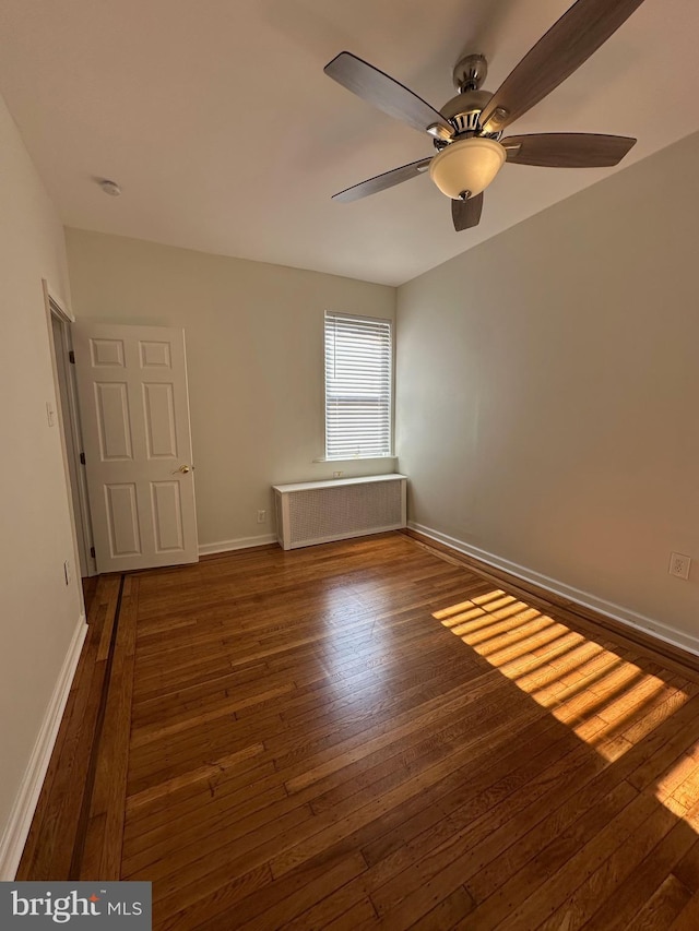 empty room featuring baseboards, hardwood / wood-style floors, and radiator heating unit