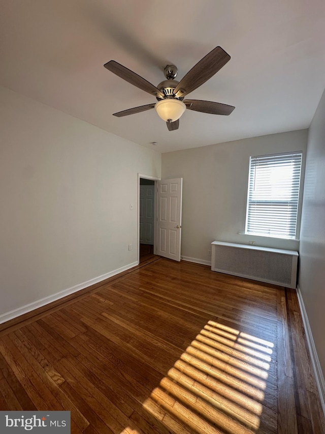 unfurnished bedroom featuring baseboards, radiator, hardwood / wood-style floors, and a ceiling fan