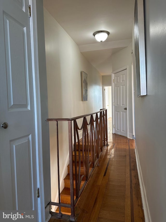 corridor featuring baseboards, an upstairs landing, and dark wood-style flooring