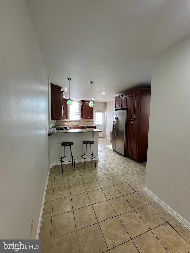 kitchen featuring a breakfast bar, stainless steel refrigerator with ice dispenser, decorative light fixtures, a peninsula, and light tile patterned floors