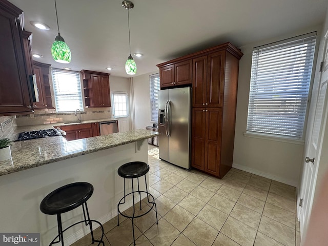 kitchen with a sink, decorative light fixtures, tasteful backsplash, stainless steel appliances, and a peninsula