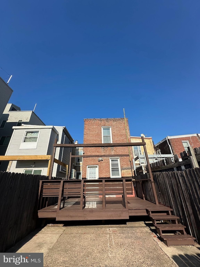 rear view of house with brick siding, a deck, and fence