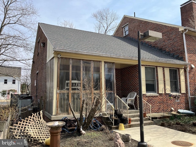 back of house featuring a sunroom, brick siding, and a shingled roof