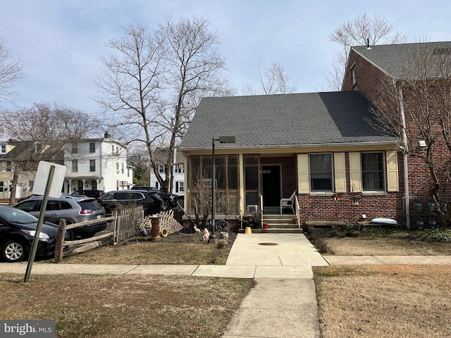 view of front of home featuring brick siding, a shingled roof, and a sunroom