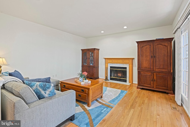 living area with recessed lighting, a premium fireplace, visible vents, and light wood finished floors