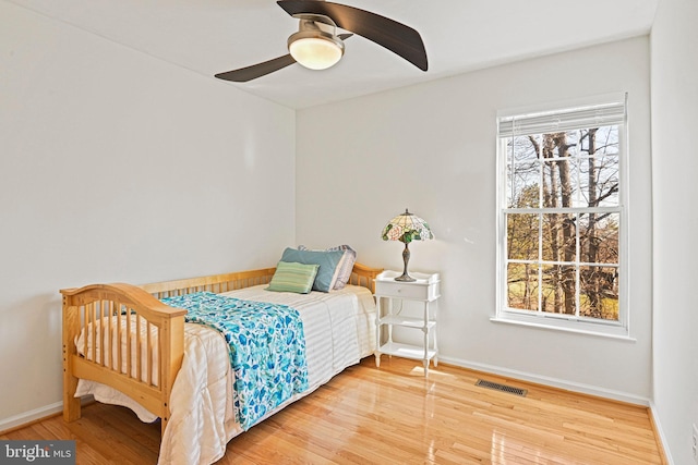 bedroom with ceiling fan, visible vents, baseboards, and wood finished floors