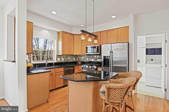 kitchen featuring backsplash, light wood-type flooring, appliances with stainless steel finishes, washer / clothes dryer, and a sink