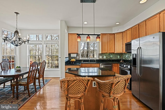 kitchen with light wood-type flooring, a notable chandelier, a sink, backsplash, and stainless steel appliances