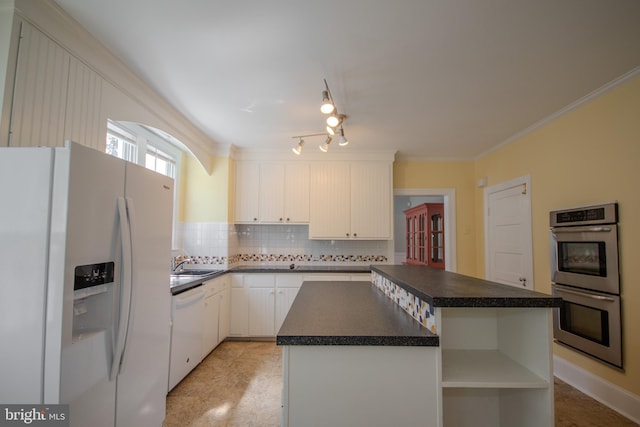 kitchen featuring dark countertops, tasteful backsplash, a kitchen island, white appliances, and a sink