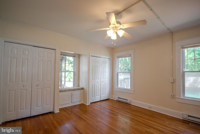 unfurnished bedroom featuring visible vents, multiple closets, ornamental molding, wood finished floors, and a baseboard radiator