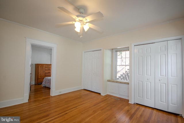 unfurnished bedroom featuring light wood finished floors, visible vents, crown molding, baseboards, and multiple closets