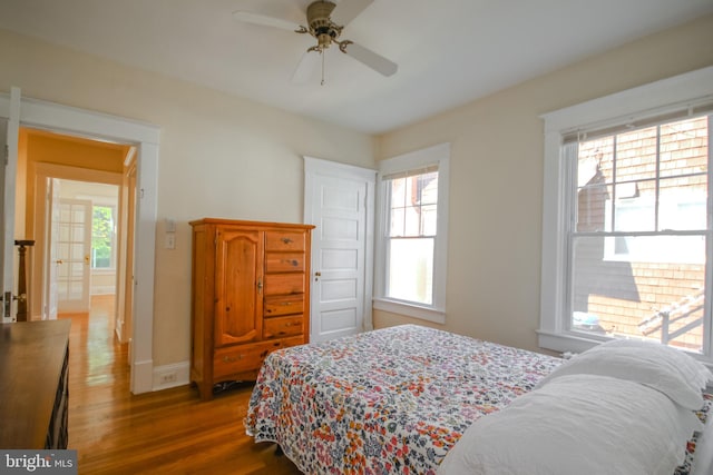 bedroom with baseboards, multiple windows, wood finished floors, and a ceiling fan