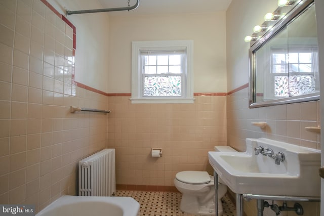 bathroom featuring a washtub, radiator, toilet, and tile walls