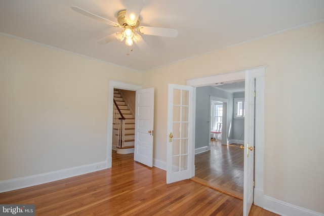 spare room with light wood finished floors, ceiling fan, stairs, and baseboards