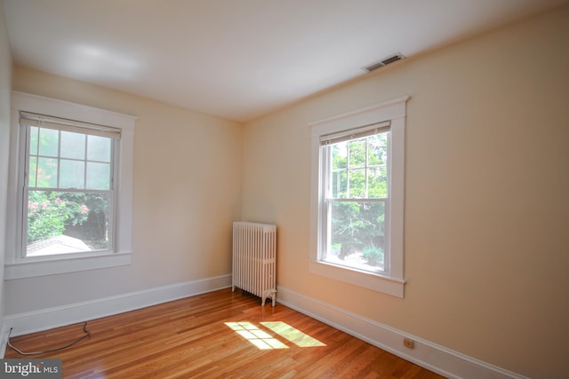 spare room featuring radiator, wood finished floors, visible vents, and baseboards