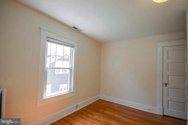 spare room featuring visible vents, radiator, baseboards, and wood finished floors