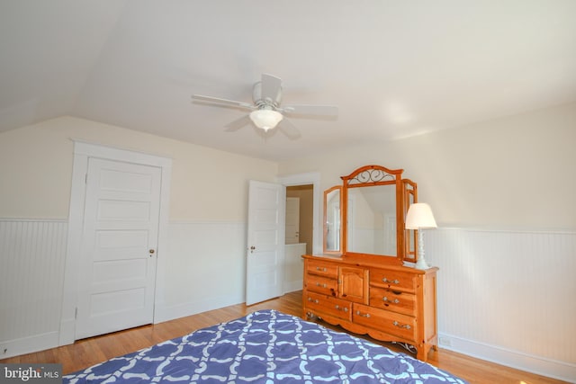 bedroom with a ceiling fan, lofted ceiling, wood finished floors, and a wainscoted wall