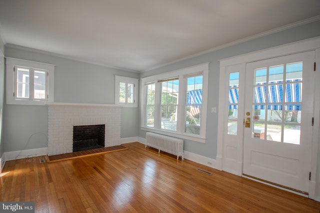 unfurnished living room featuring visible vents, ornamental molding, wood-type flooring, radiator, and a brick fireplace