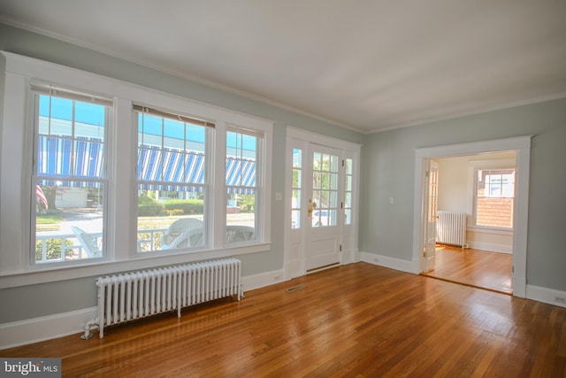 empty room with radiator, wood finished floors, baseboards, and ornamental molding