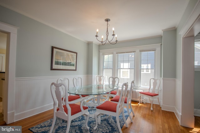 dining room featuring an inviting chandelier, crown molding, wood finished floors, and a wainscoted wall